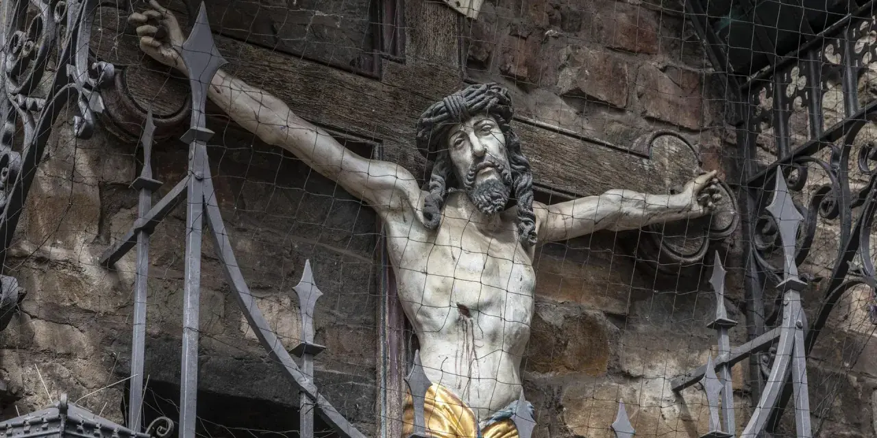 Kreuzigungsgruppe mit Jesus, der die Frage aufwirft, wie alt war Jesus als er starb. Davor ein schmiedeeiserner Zaun.