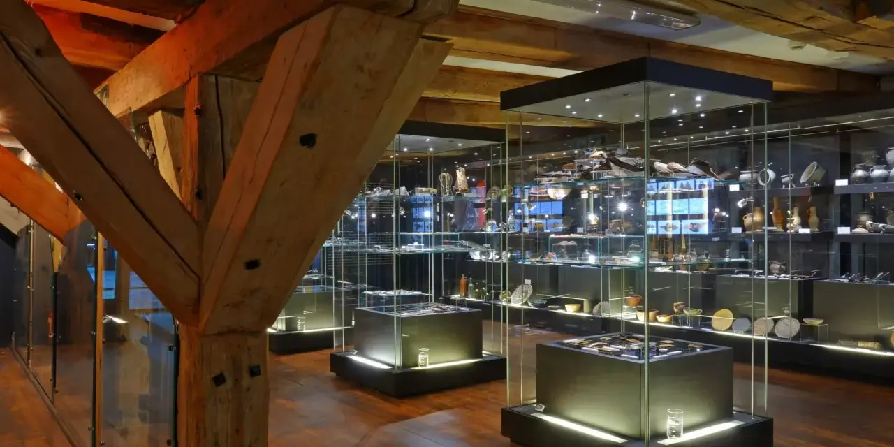 Wnętrze muzeum z zabytkowymi belkami i przeszklonymi gablotami pełnymi artefaktów. Może tu jest też błękitny baranek?