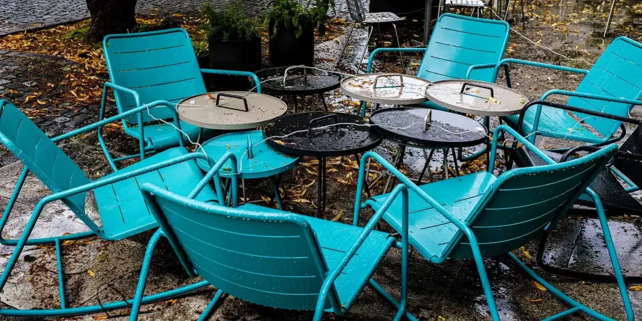 Teal metal chairs and tables, perfect for outdoor use, sit empty on a wet patio.
