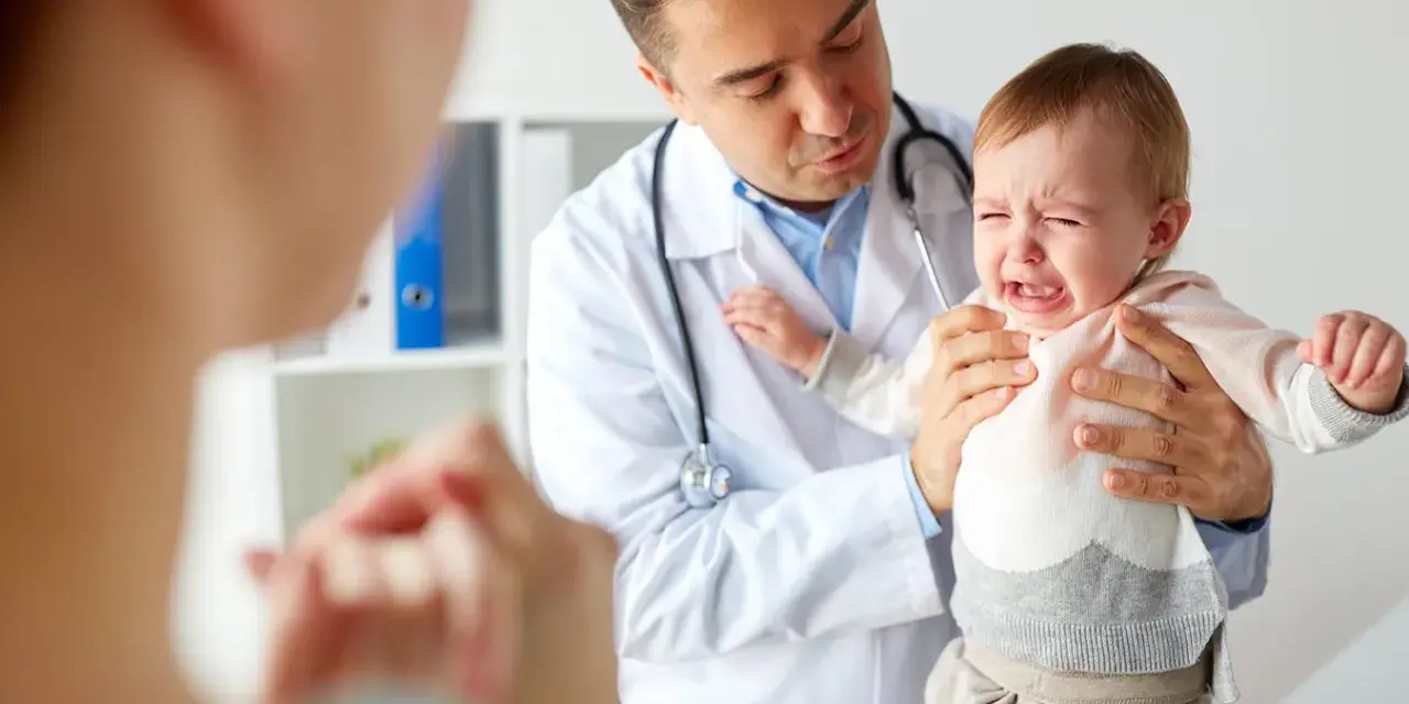 Lekarz uspokaja płaczące dziecko, które przechodzi skok rozwojowy 4 latka. Mama wspiera malucha.