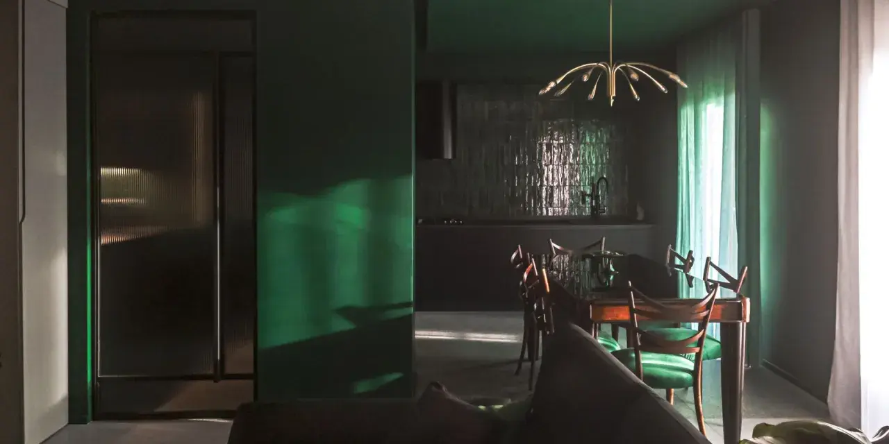 Un soggiorno moderno con pareti verde scuro, un divano antracite e una zona pranzo con sedie verdi. I colori da abbinare al verde scuro sono il legno scuro e l'ottone.