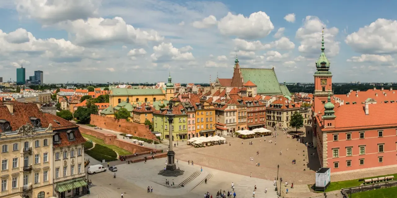 Uroczy city break z Warszawy. Rynek Starego Miasta tętni życiem, z kolorowymi kamieniczkami i Zamkiem Królewskim w tle.