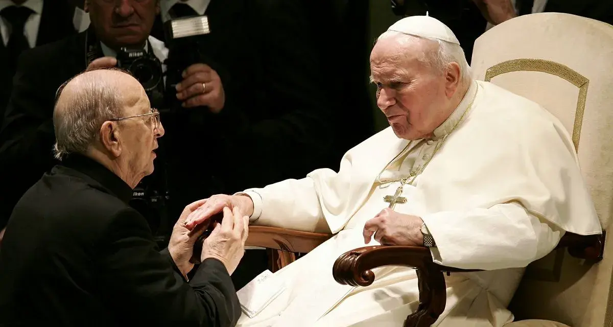 Papież Jan Paweł II w białej szacie, klęczący mężczyzna w czerni. W tle widać fotografów. To obraz duchowej siły, jakiej doświadczają legiony Chrystusa.
