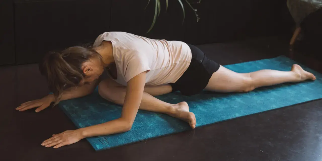 Femme en posture de pigeon sur un tapis bleu, un excellent exercice pour le dos à la maison.