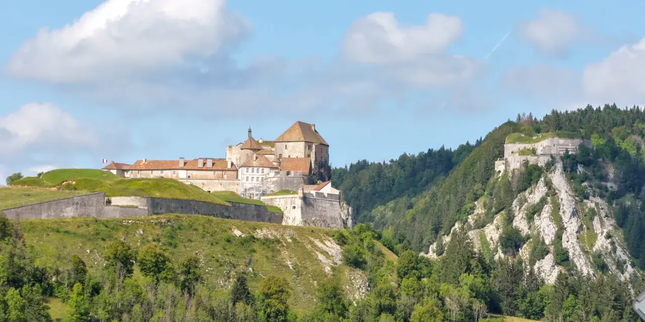 Fort de Joux, un site historique à visiter dans le Doubs, perché sur une colline verdoyante sous un ciel bleu.