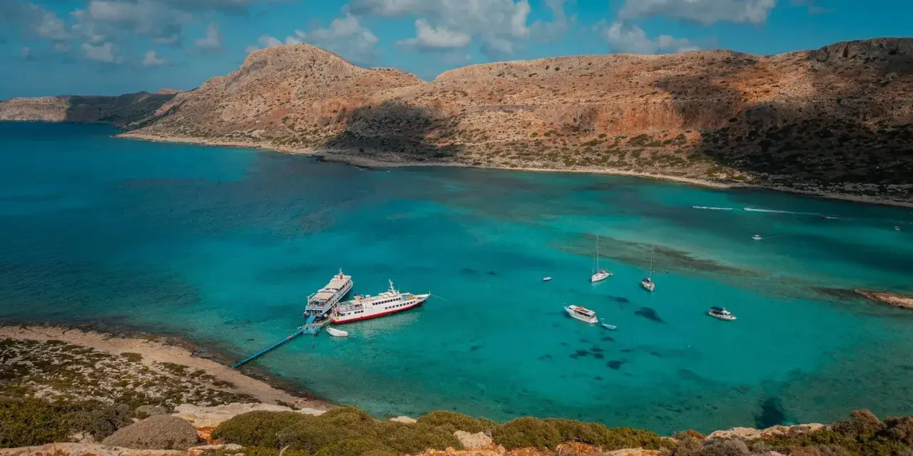 Wycieczka na Santorini z Krety: statki cumują w turkusowej zatoce, otoczonej skalistymi wzgórzami.