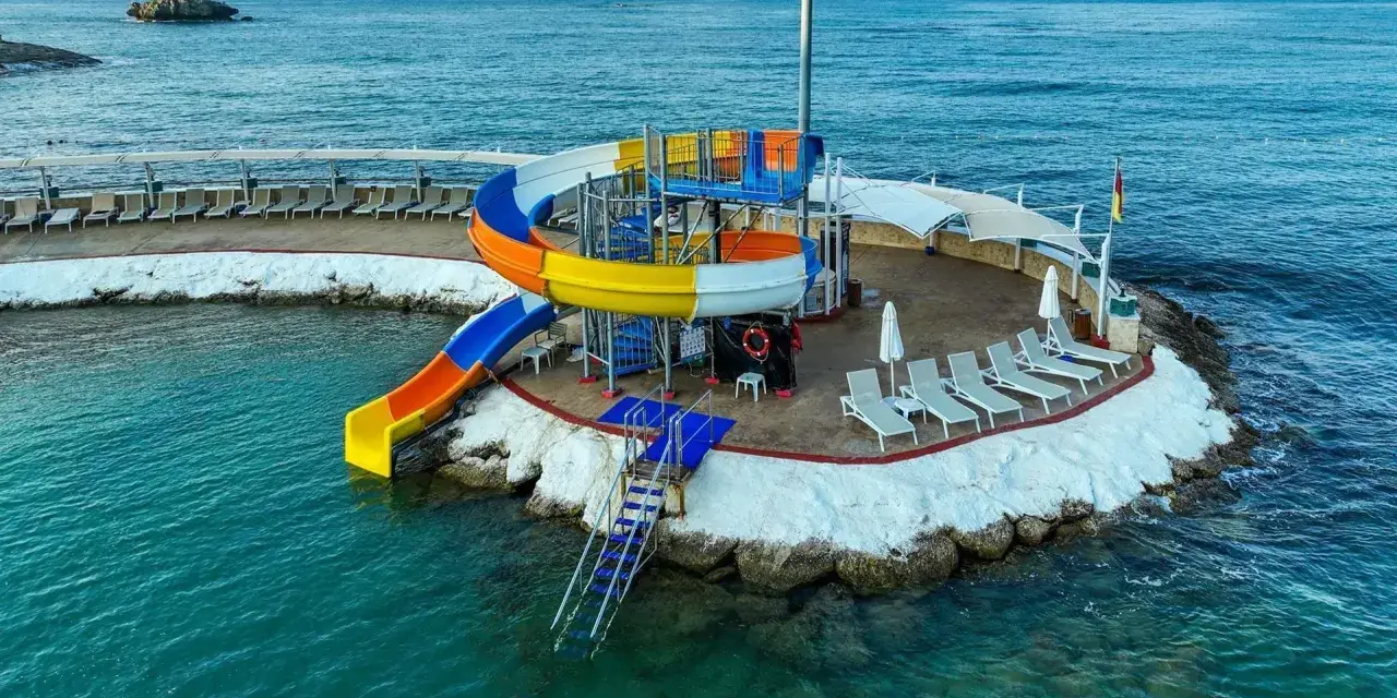 Kolorowe zjeżdżalnie wodne i leżaki na wyspie w Orange County Alanya, nad turkusowym morzem.