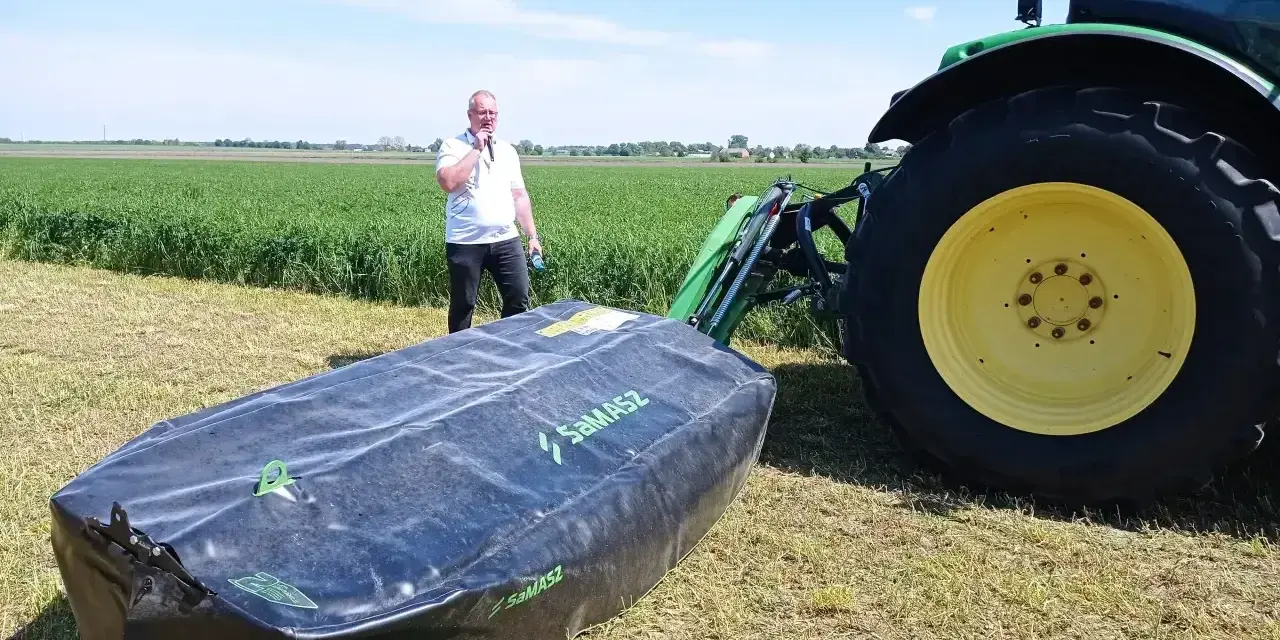 Mężczyzna prezentuje nowoczesne kosiarki dyskowe SaMASZ obok zielonego traktora na polu.