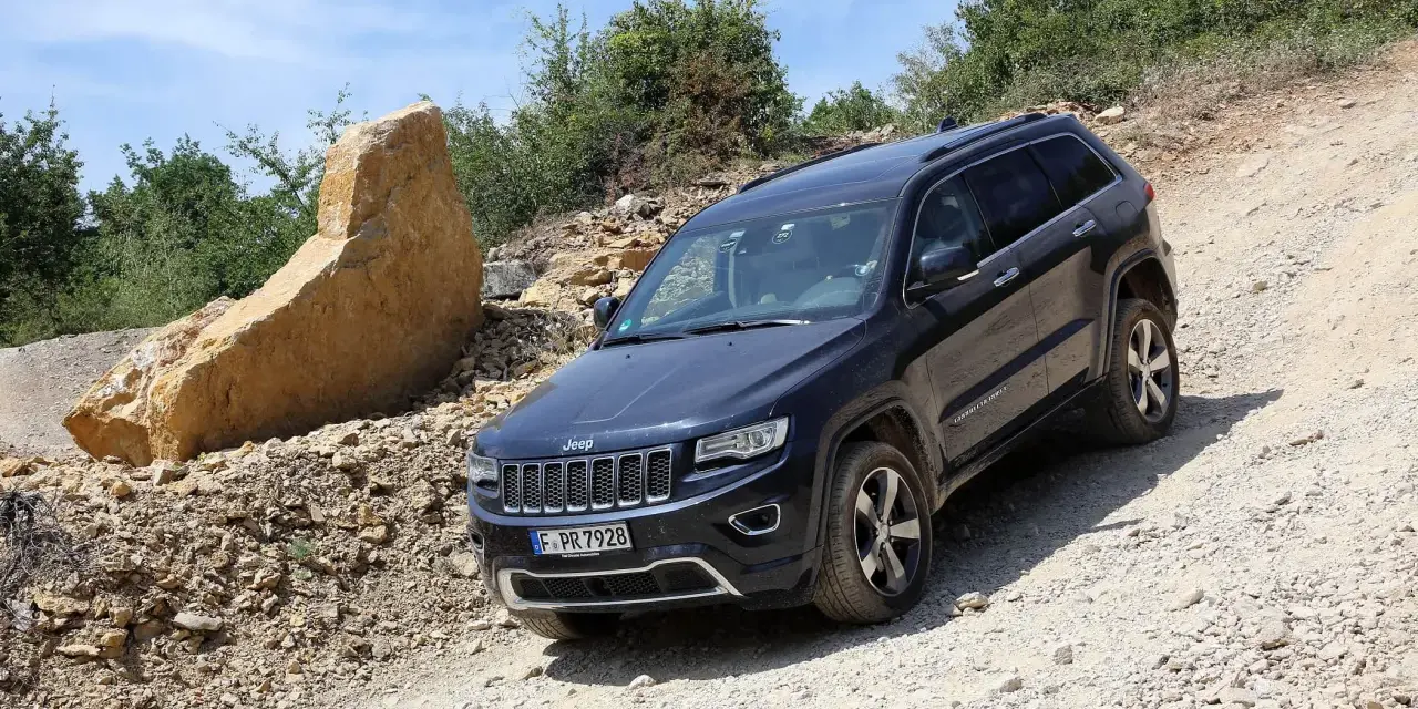 Schwarzer Jeep Grand Cherokee 3.0 CRD 250 PS im Gelände. Ein großer Felsbrocken liegt daneben.