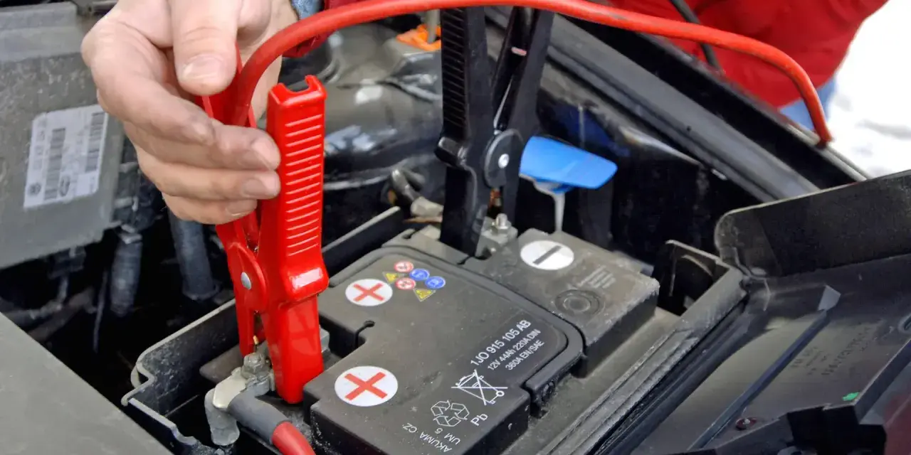 Hand befestigt rote Klemme an Autobatterie. Die richtige **Starthilfe Reihenfolge** ist entscheidend für die Sicherheit.