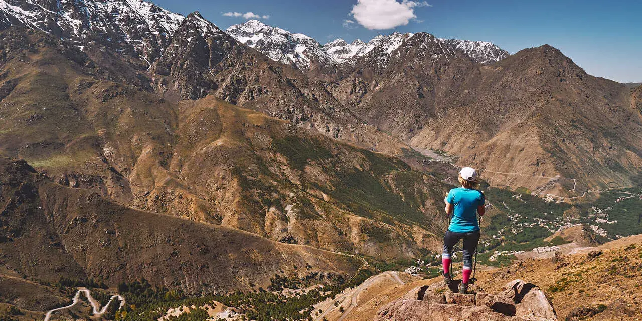 Widok na ośnieżone szczyty górskie Jebel Toubkal. Turystka podziwia panoramę z skalistego zbocza.
