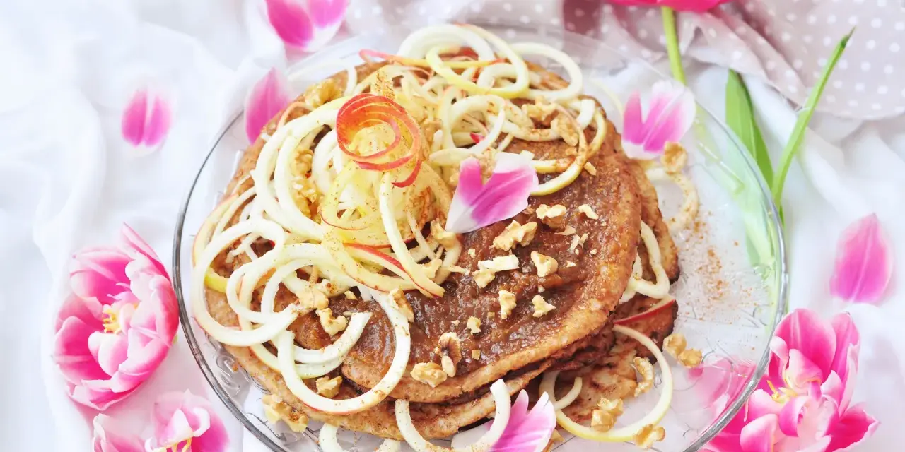 En vacker pannkakstårta med äpple, kanel och valnötter, perfekt för ett pannkakstårta recept. Omgiven av rosa tulpaner.