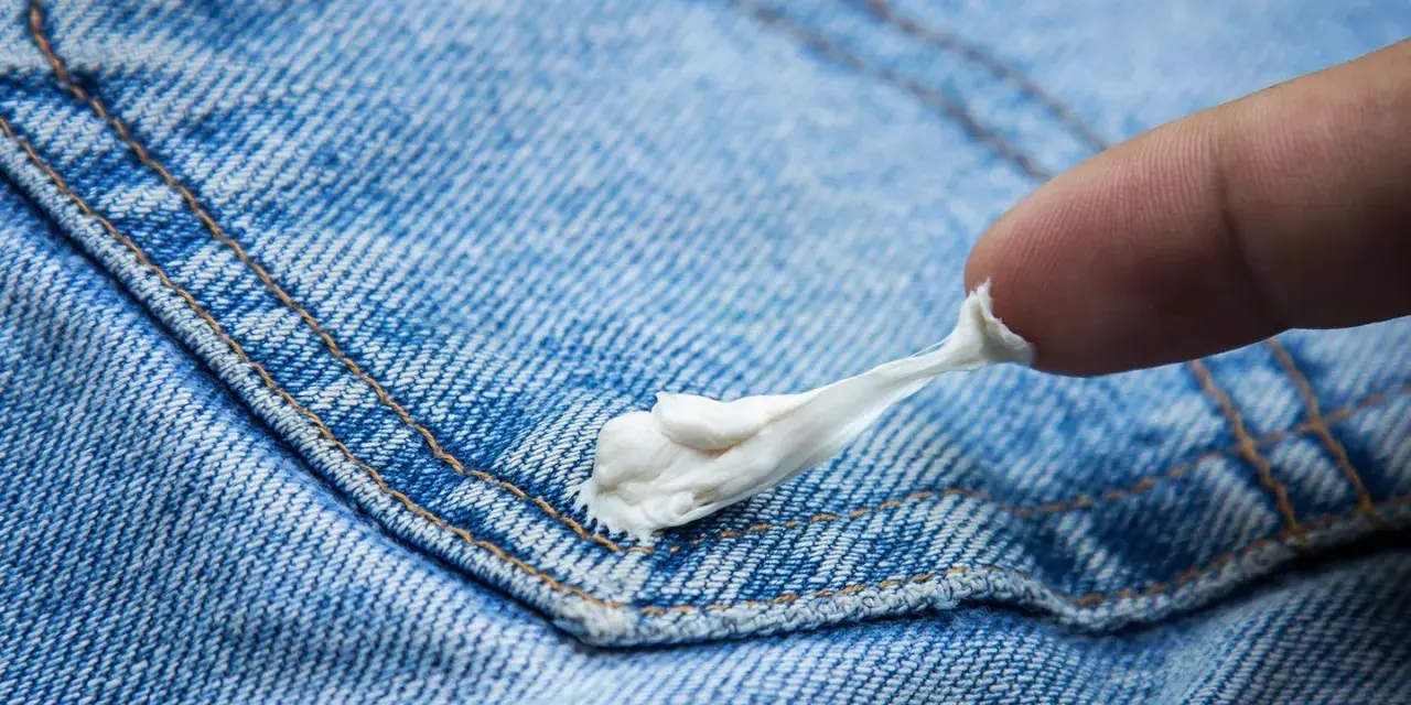 Ein Finger versucht, Kaugummi von Jeans zu entfernen. Der klebrige Kaugummi zieht sich zäh.