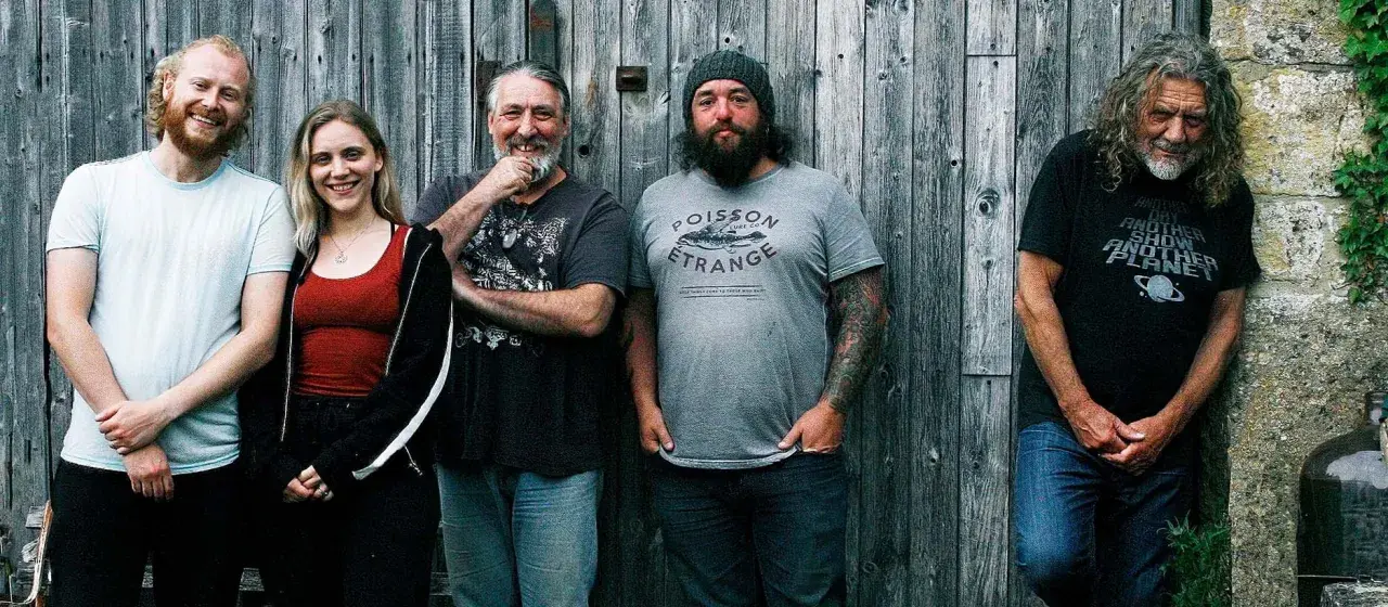 Le groupe de Robert Plant, avec ses musiciens, pose devant un mur de bois.