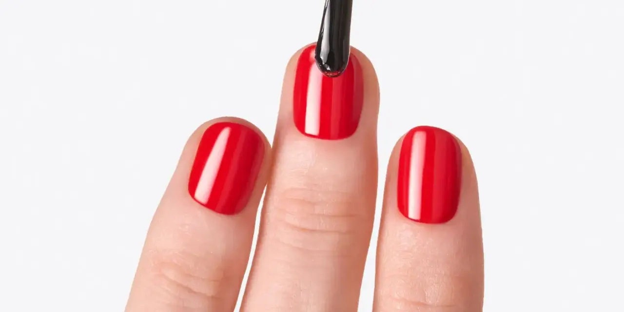 Application d'un top coat sur des ongles rouges brillants. Le top coat, c'est quoi ? C'est la touche finale pour une manucure parfaite.
