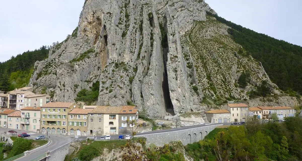 Imponerande klippformation vid Route Napoléon. En by klättrar uppför bergssluttningen, med en bro och en turkos flod nedanför.