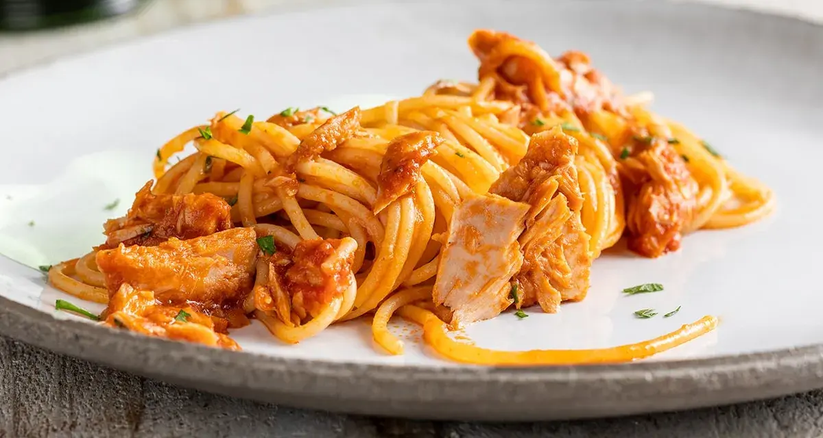 Spaghetti al tonno conditi con un sugo saporito e ricchi pezzi di tonno, guarniti con prezzemolo fresco.