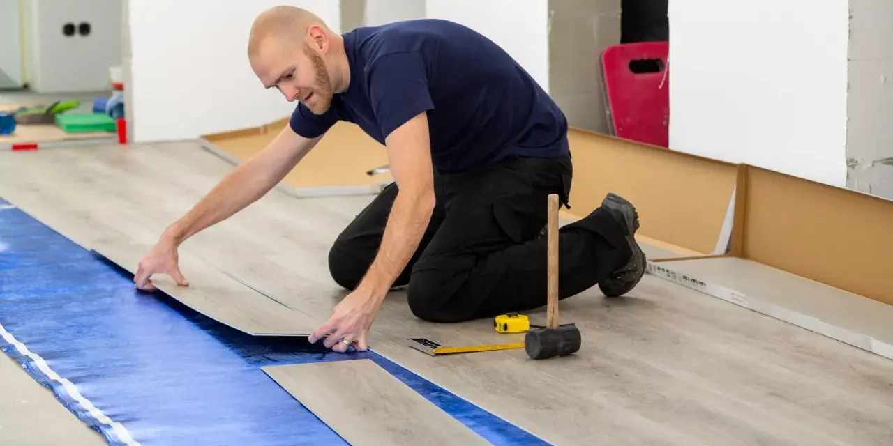 Pose d'un revêtement de sol stratifié sur une sous-couche d'isolation phonique sous carrelage. Outils de pose à proximité.