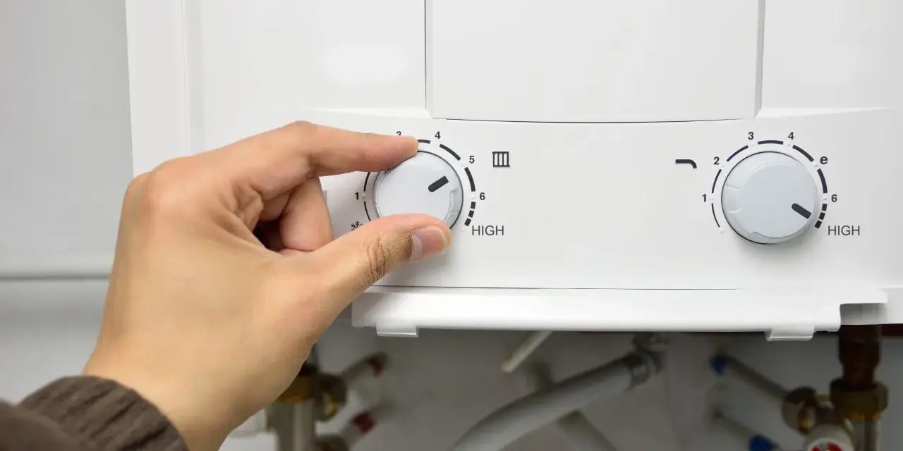 Mano girando el dial del termo eléctrico para cerrar la llave de paso.