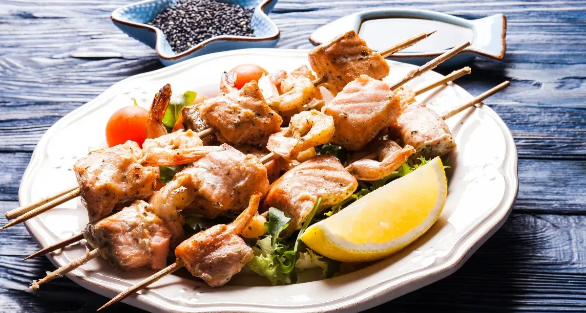 Spiedini di pesce succulenti, con gamberi e salmone grigliato, serviti su un letto di insalata con spicchio di limone.