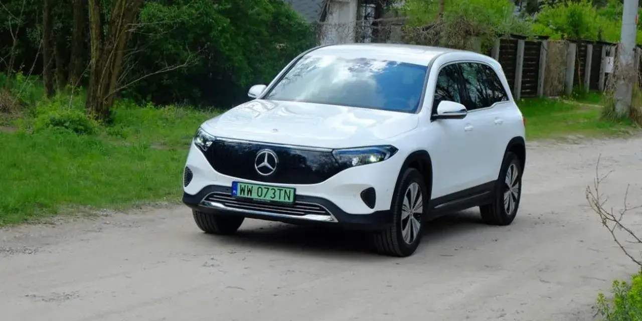 Biały Mercedes EQB na drodze gruntowej, otoczony zielenią.