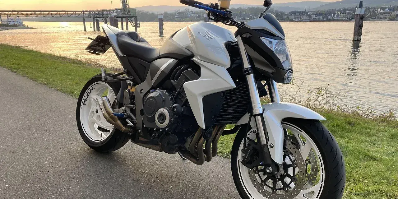 Biały motocykl Honda CB1000R, model a2 motor, zaparkowany nad rzeką o zachodzie słońca.