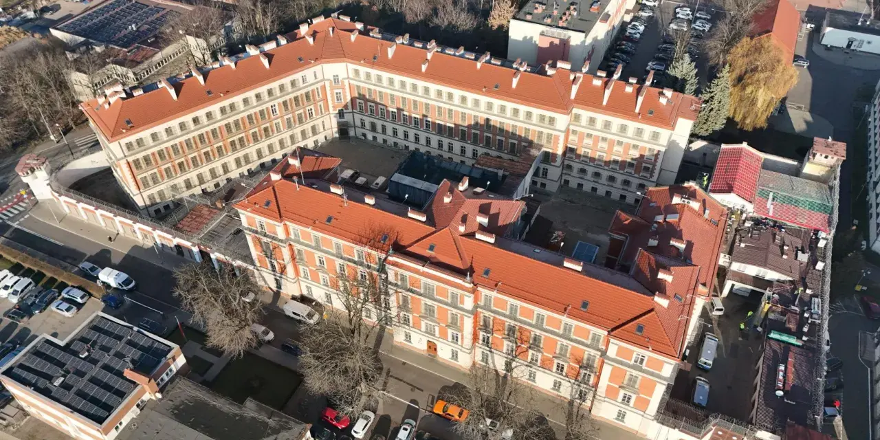 Widok z lotu ptaka na zakład karny Montelupich. Widać budynki z czerwonymi dachami, ogrodzenie z drutem kolczastym i parking. Odwiedziny w zakładzie karnym.