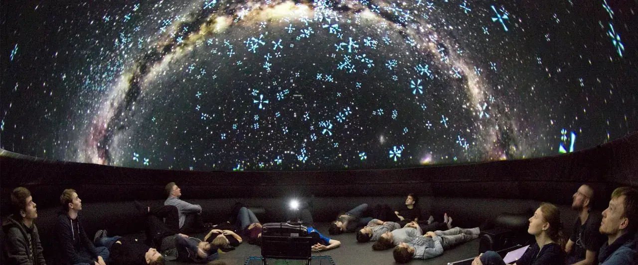 Besucher im Planetarium Berlin liegen und sitzen und blicken gebannt auf die Projektion der Milchstraße und funkelnder Sterne.