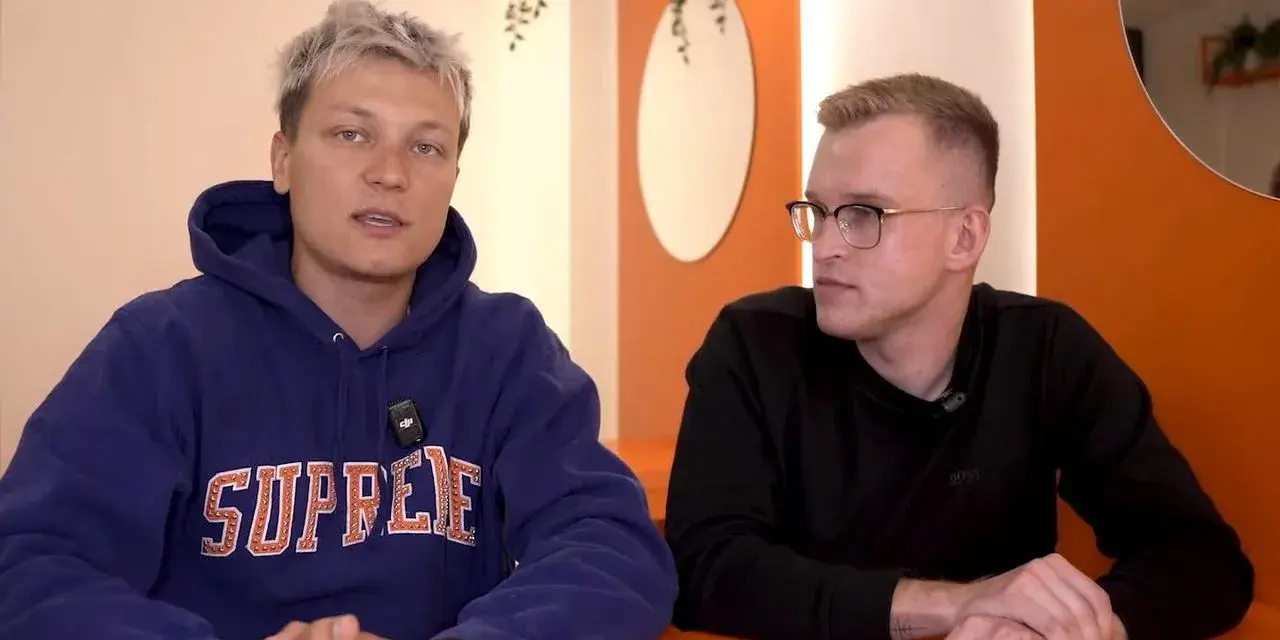 Dwóch mężczyzn siedzi przy pomarańczowym stole. Jeden w niebieskiej bluzie z napisem "SUPREME", drugi w czarnej koszulce. Rozmawiają o kebabie friza.
