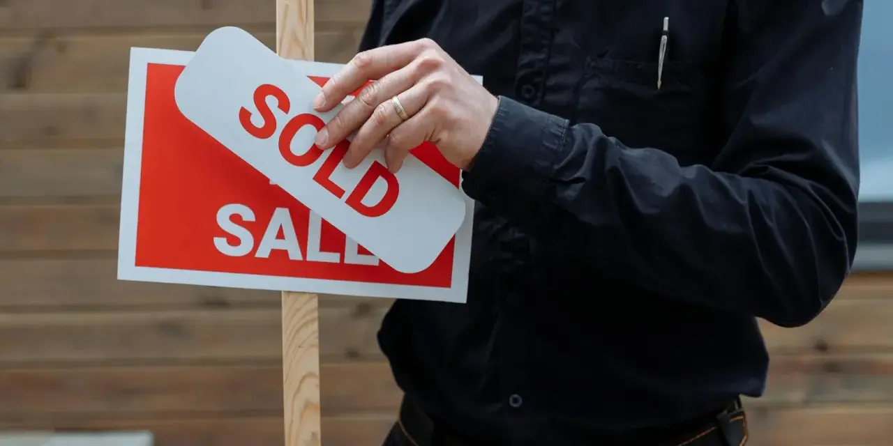 Hombre coloca cartel de "Vendido" sobre uno de "En Venta". Una venta rápida, quizás por debajo del valor de referencia.