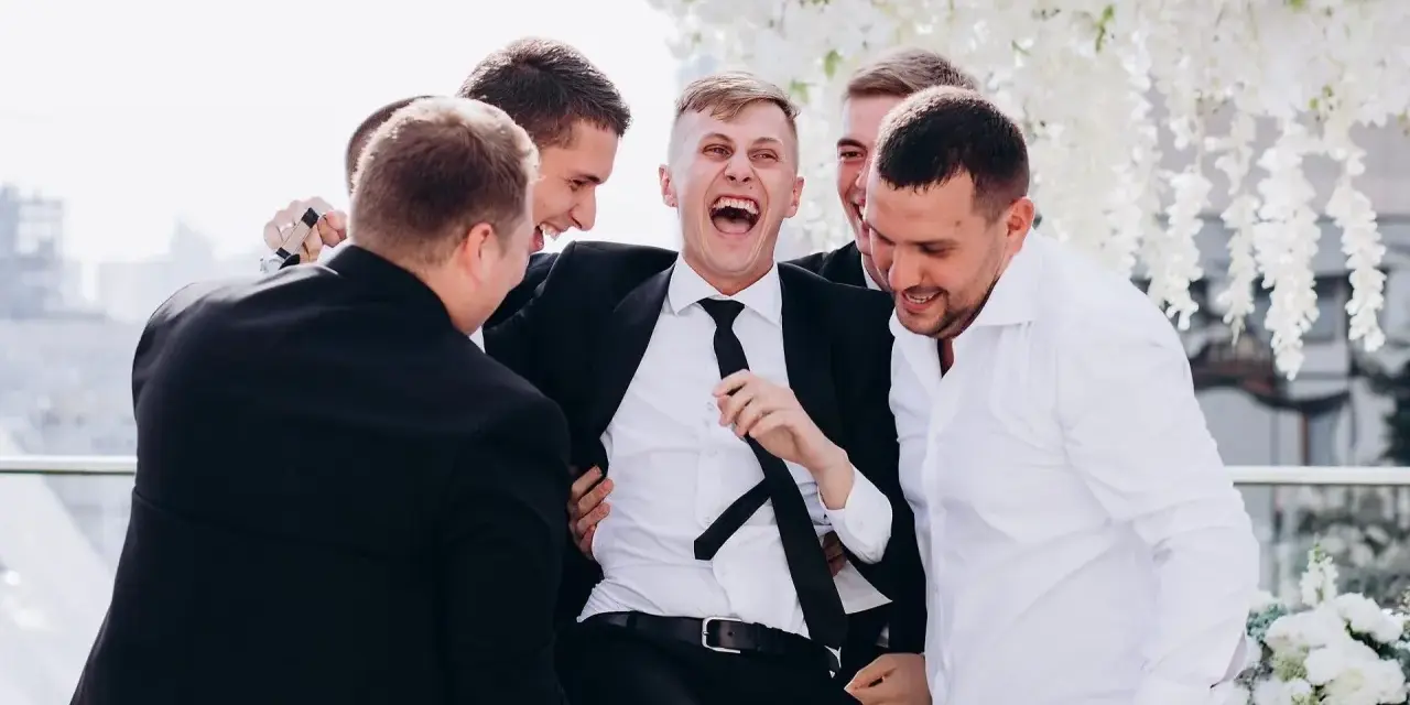 Śmiejący się pan młody otoczony przez przyjaciół. Świetne kawalerski pomysły na wspólne chwile przed ślubem.