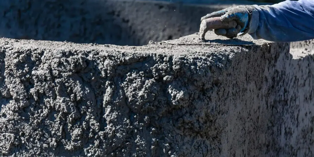 Ręka w rękawicy wygładza świeży beton. Zastanawiasz się, ile kosztuje worek cementu na budowie?
