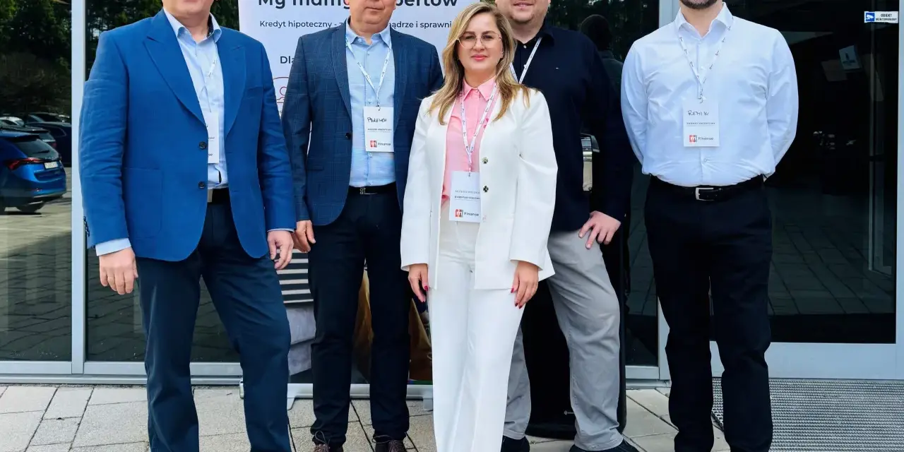 Pięć osób w eleganckich strojach stoi przed budynkiem z banerem "m Finanse".