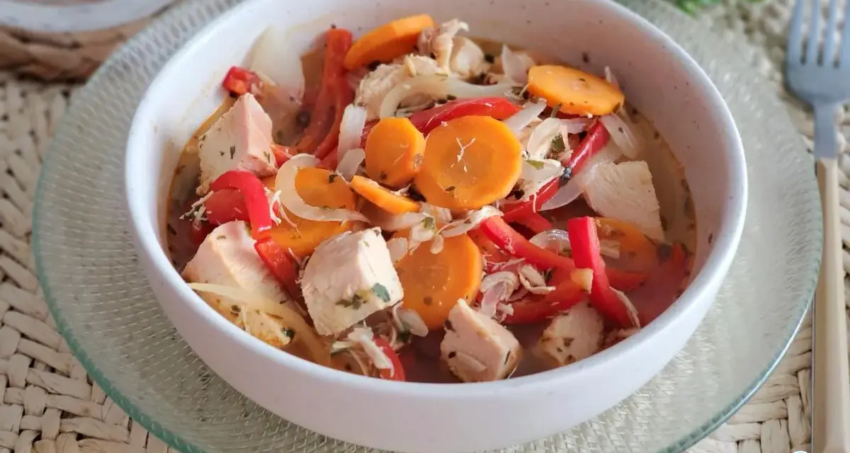 Pechuga de pollo en escabeche con zanahoria, pimiento rojo y cebolla, servida en un cuenco blanco sobre una base tejida.