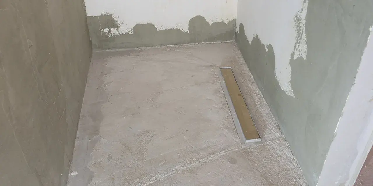 Niedawno położony szlam mineralny w łazience, z widocznym odpływem liniowym. Ściany w trakcie tynkowania.