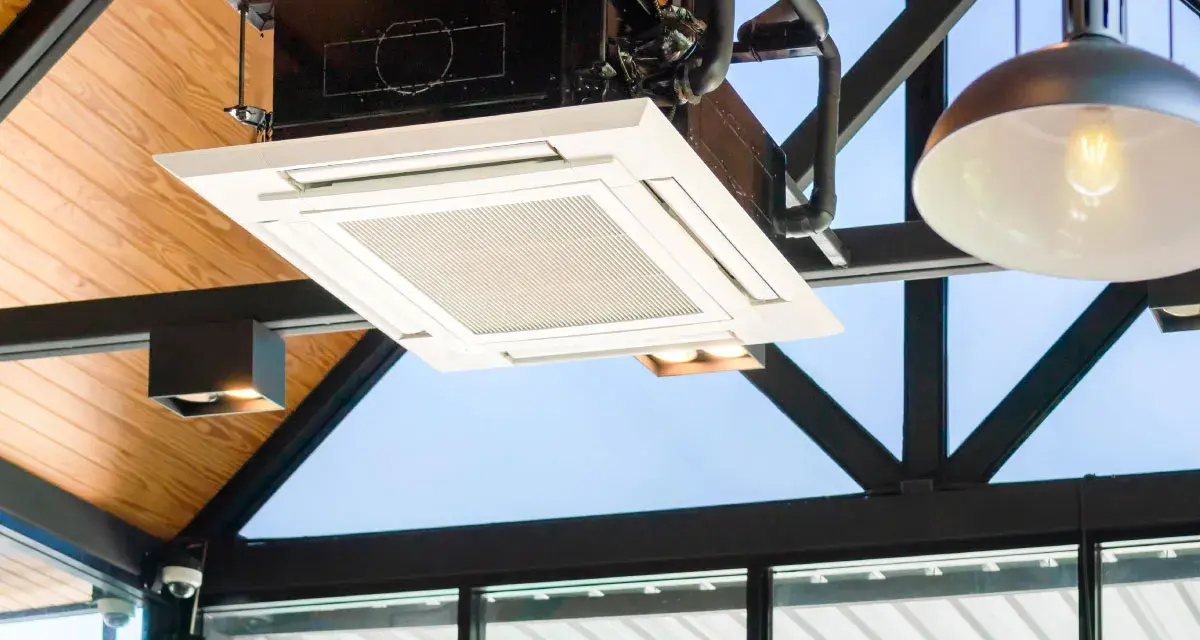 Unidad de cassette de un sistema VRV integrada en un techo de madera y metal, con luces y tuberías visibles.