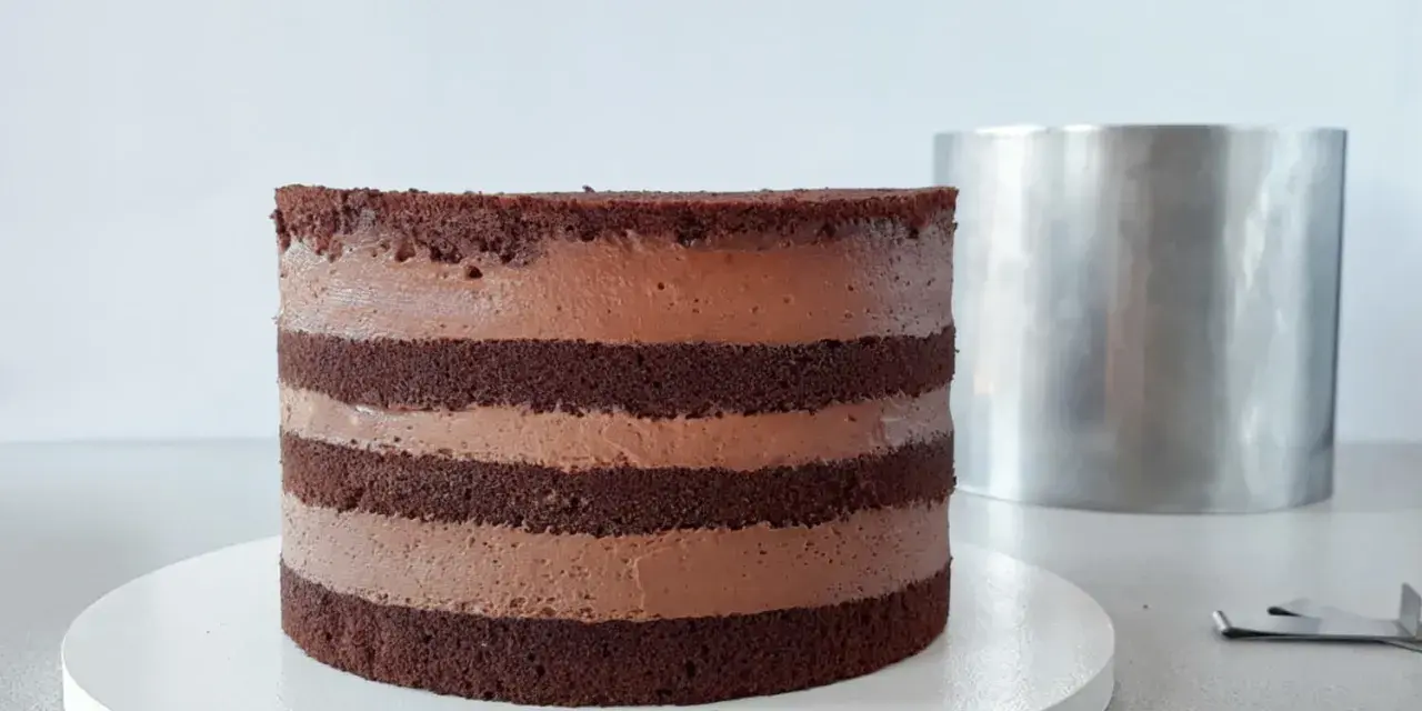 Czekoladowy tort bomba z kremem, gotowy do dekoracji. Obok metalowa obręcz.