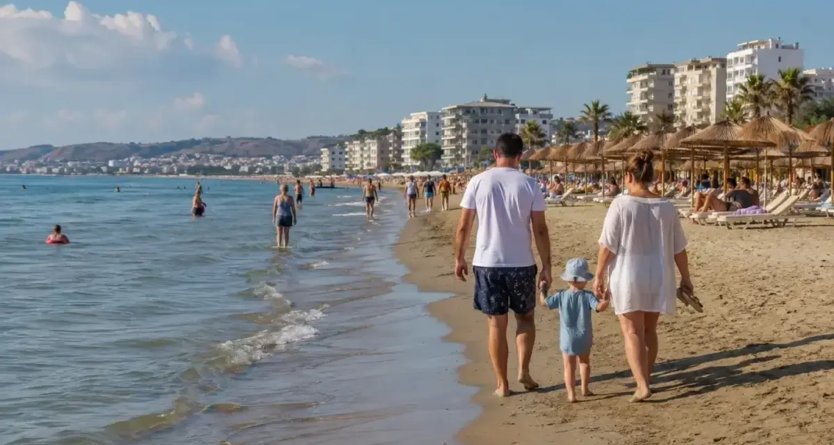 Rodzina spaceruje po piaszczystej plaży w Durrës. W tle widać morze, budynki i parasole plażowe.