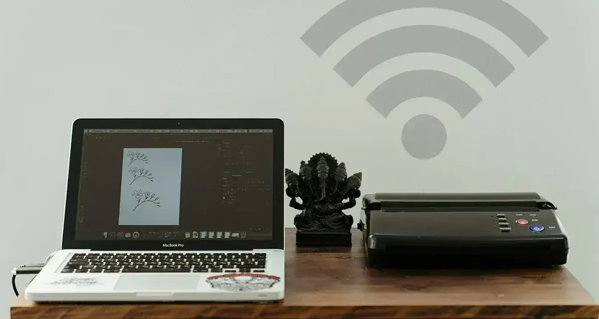 Laptop z projektem graficznym i drukarka obok figurki Ganesha. Symbol Wi-Fi nad nimi sugeruje bezprzewodowe drukowanie.