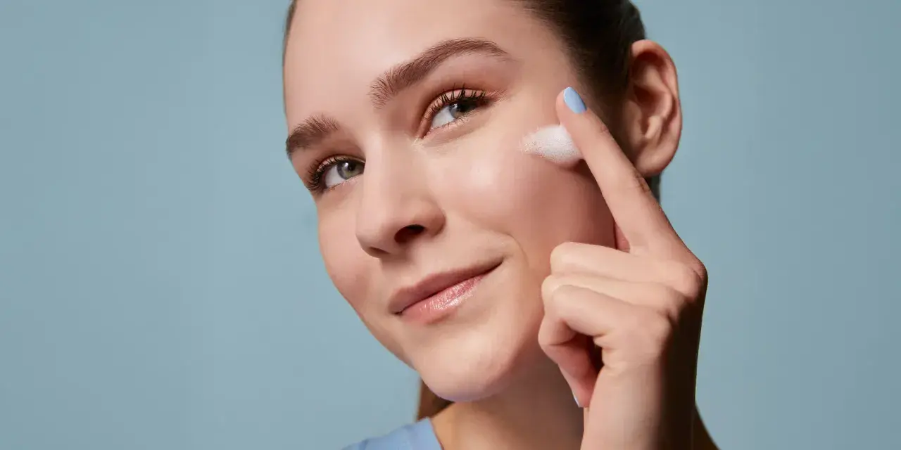 Donna applica schiuma sul viso, un gesto essenziale per la skincare routine mattina e sera. Pelle luminosa e curata.