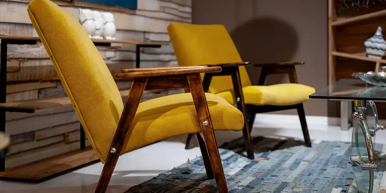 Due poltrone gialle con struttura in legno scuro, un tappeto patchwork e un tavolino in vetro. Un tocco di arredamento anni '70 italiano.