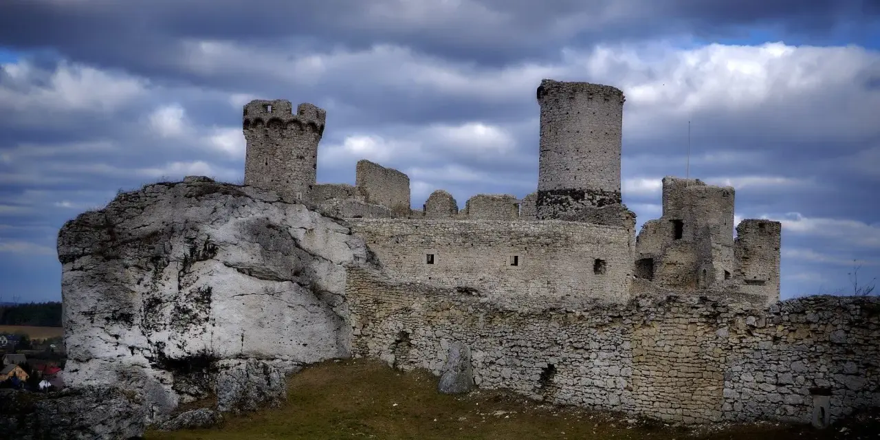 Ruiny zamku Ogrodzieniec na skale, z wieżami i murami, pod burzowym niebem. Idealne miejsce na trasę pełną historii.