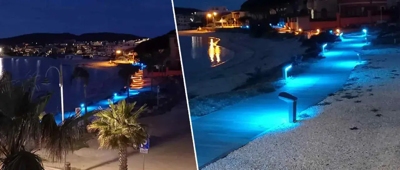 Passeggiata illuminata da luci blu sul lungomare di Golfo Aranci sera, con palme e case sullo sfondo.