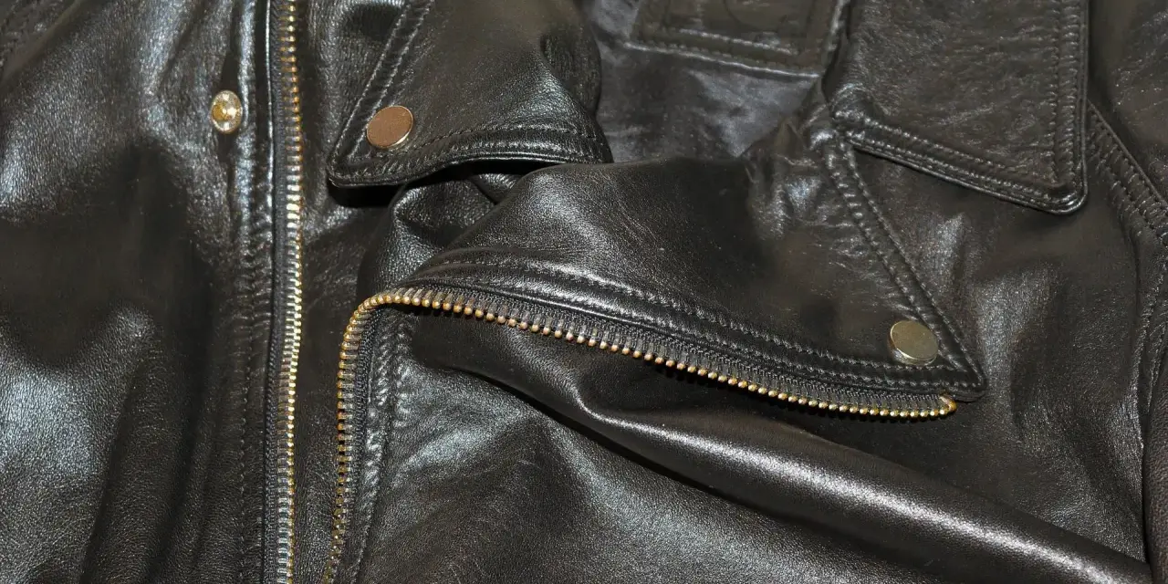Dettaglio di una giacca in ecopelle nera con zip dorata e bottoni a pressione. Si pensa a come lavare giacca ecopelle in lavatrice.