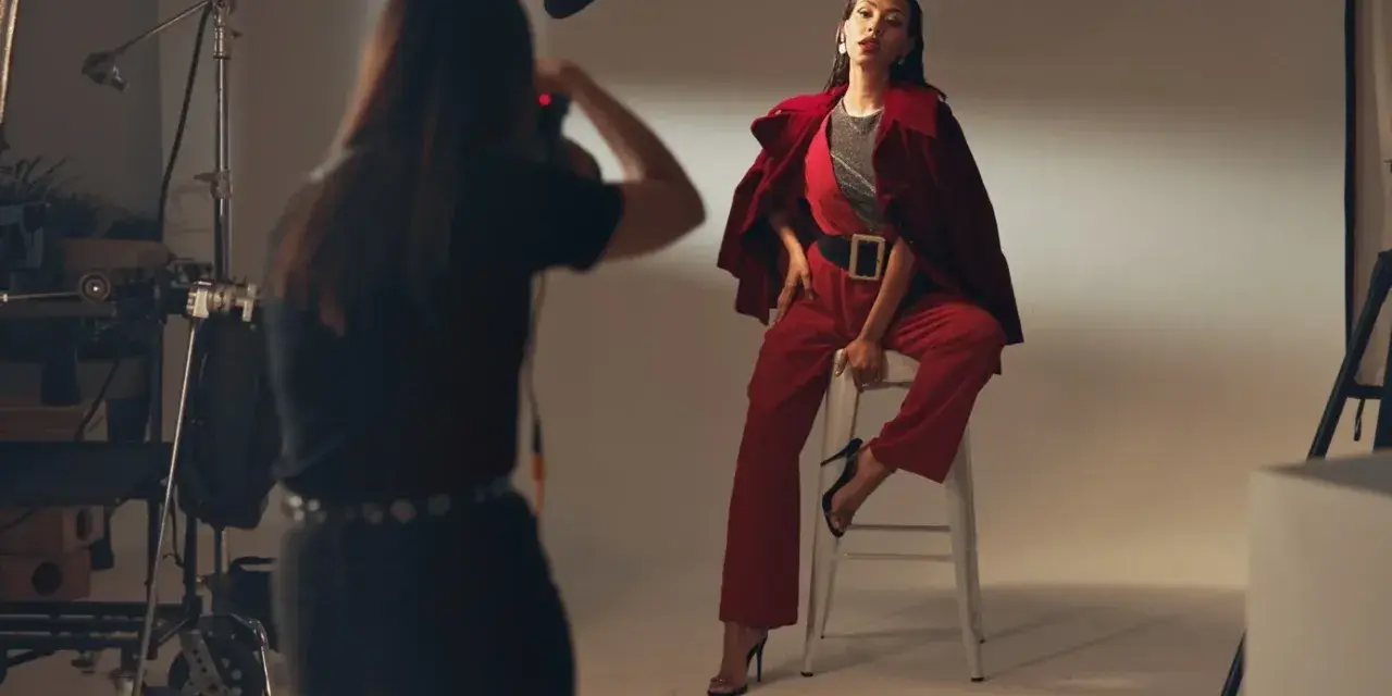 Sesja zdjęciowa w studio. Modelka w czerwonym stroju pozuje na stołku. Fotografka robi zdjęcie. Zastanawiasz się, ile zarabia fotograf?