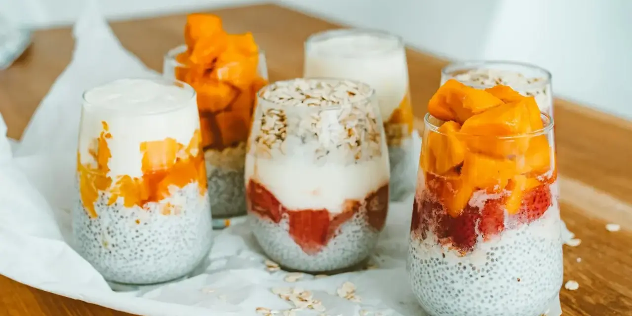 Pyszny deser chia z mango i truskawkami w szklankach, ułożony warstwowo z jogurtem i płatkami owsianymi.