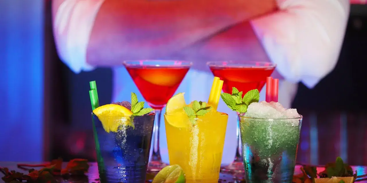 Kolorowe drinki z owocami i miętą na barze, w tle barman.