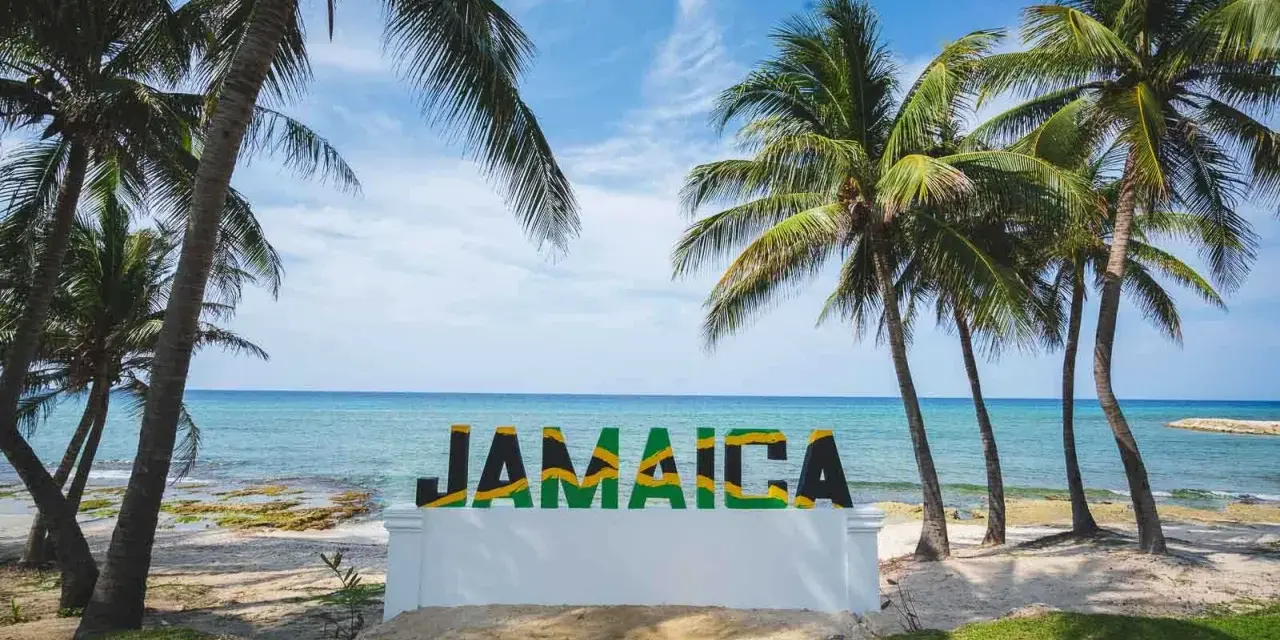 Napis "JAMAICA" na tle plaży, morza i palm.
