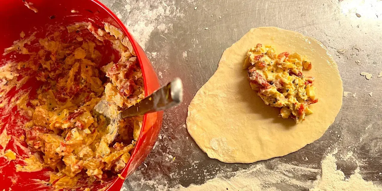Fyllning till piroger recept läggs på deg. En röd skål med fyllning syns till vänster.