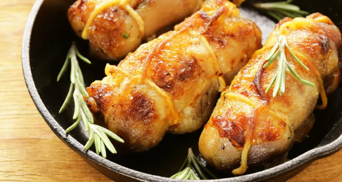 Involtini di pollo dorati e succulenti, legati con spago da cucina e guarniti con rametti di rosmarino, in una padella di ghisa.